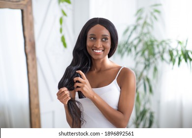 Hair Care Cosmetic. Happy Millennial African American Female Apply Hair Care Spray Product On Ends, Split Tips, Treatment Dry Hair Or Sun Protection At Home In Bedroom Interior With Plant In Morning