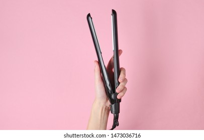 Hair Care. Female Hand Holding Hair Straightener On Pink Background. Top View