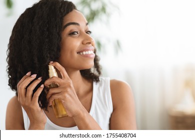 Hair Care. Happy Afro Woman Using Oil For Split Ends While Getting Ready At Home, Closeup Image With Copy Space