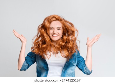 Hair Care. Portrait of cheerful redhead girl with flying curly hair, laughing at camera, having fun on gray background.