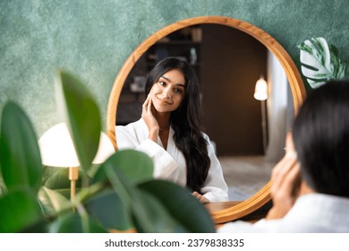 Hair care and self-care with beautiful Indian woman looking in mirror touching her healthy long hair sitting at the dressing table. - Powered by Shutterstock