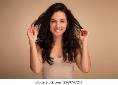 Hair Care And Therapy Treatment Concept. Portrait of smiling indian woman posing and touching dark long hair. Beautiful millennial lady standing isolated over beige studio background, copy space - Powered by Shutterstock