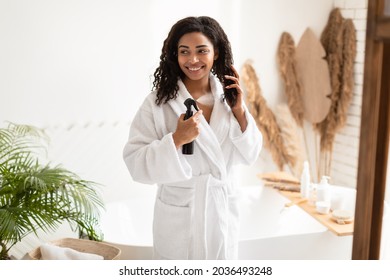 Hair Care Treatment. African American Woman Spraying Hairspray Moisturizing Wet Curly Hair After Shower Standing In Modern Bathroom At Home, Looking Aside. Haircare Cosmetics Concept