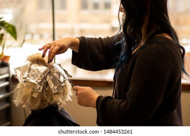 Hair color application on a woman with blonde hair by a professional stylist at a salon