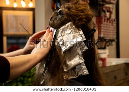 Hair color application on a young blonde woman by a professional hair stylist at a salon 