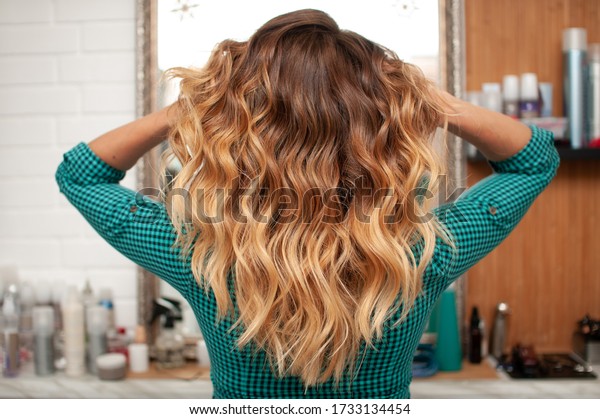 Hair coloring gradient from light\
golden to brown on a girl with long curly hair in the\
back