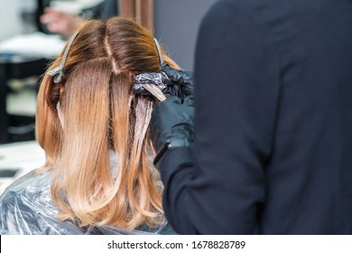 Hair coloring of young woman by hands of hairstylist close up.