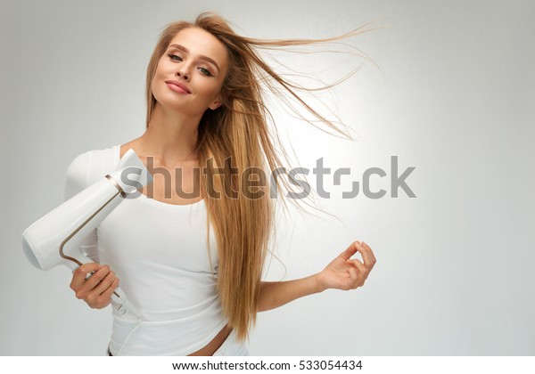 ヘアドライヤー ヘアドライヤーを使って 金髪のまっすぐな髪の美しい笑顔の女の子 ブローヘアドライヤーを使用した幸せな女性のポートレート 髪型 ヘアケアのコンセプト 高解像度 の写真素材 今すぐ編集