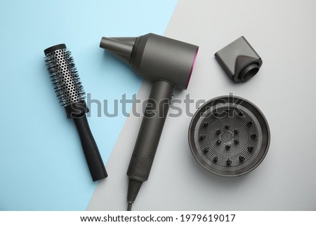 Hair dryer with nozzles and round brush on color background, flat lay