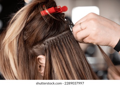Hair extensions in a beauty salon, using capsules, girl at the hairdresser, hair clips, professional equipment, light blond hair, close-up, process, change of hairstyle on head