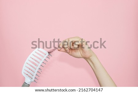 hair fall out concept. isolated hands with hair brush and another hand drags hair clump from brush. pink background.postpartum hair loss, hormonal disbalance.mockup,free space