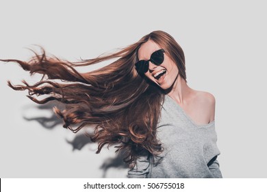 Hair Like Fire. Attractive Young Smiling Woman In Sunglasses And With Tousled Hair Looking Away While Standing Against Grey Background