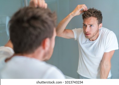 Hair Loss Man Looking In Bathroom Mirror Styling Hairstyle With Gel Or Checking For Hair Loss Or Grey Hairs. Unhappy Male Health Problem.