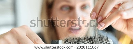 Hair loss problem and unhealthy hair. Frustrated and frightened caucasian woman holding comb with a lot of hair. Female face is defocused, hairbrush close-up.