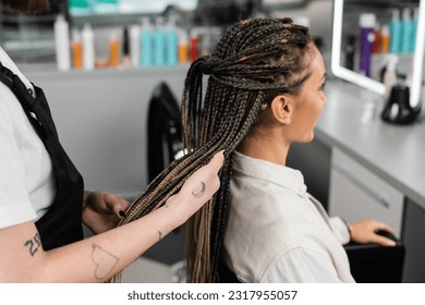 hair professional, tattooed beauty worker holding braids of female client in salon, beauty industry, salon job, customer in salon, hairdresser, salon services, hair make over