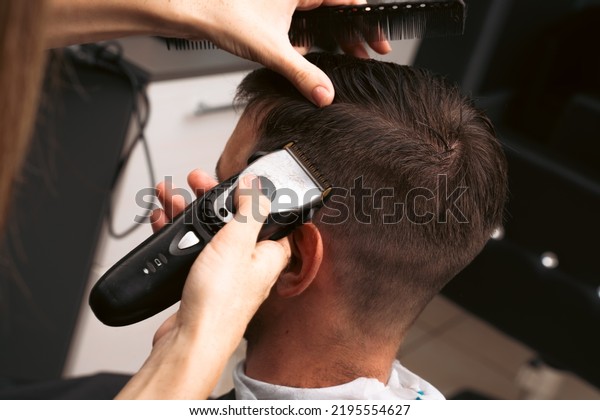 Hair salon master trimmed\
client hair with electric razor at barber shop. Male client getting\
haircut by hairdresser. Hair care, beauty industry, barber\
concept.