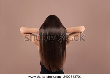 Hair styling. Woman with straight long hair on pale brown background, back view