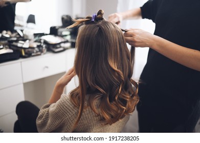 Hair stylist prepares woman makes curls hairstyle with curling iron. Long light brown natural hair - Shutterstock ID 1917238205