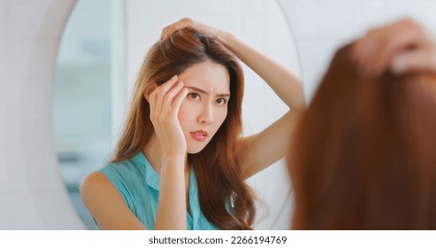 Hair treatment concept - asian annoyed woman looking in mirror has hairline receding  - Shutterstock ID 2266194769