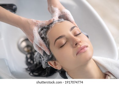 Hair Wash. Woman Looking Relaxed While Hair Stylist Washing Her Hair With Shampoo