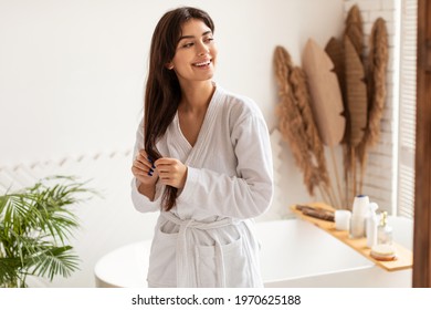 Haircare Concept. Joyful Pretty Woman In Bathrobe Touching Long Brunette Hair Standing In Modern Bathroom At Home In The Morning. Lady Enjoying Beauty Routine Caring For Herself - Powered by Shutterstock