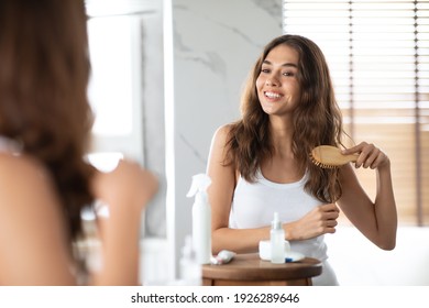 Haircare Routine. Pretty Woman Brushing Hair With Hairbrush Standing Near Mirror In Modern Bathroom At Home. Hair Combing, Healthy Beauty Care Concept. Selective Focus