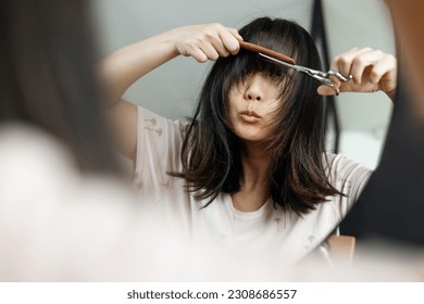 Haircut. Beautiful asian woman is going to cut her hair by herself. Women's haircut and hairdresser. Bangs hair. Close up hairstyle with bangs.