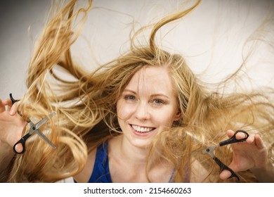Haircut coiffure haircare concept. Crazy girl with blowing long blonde hair holding scissors, showing work tools normal and thinning shears