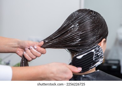 Hairdresser applies a hair mask to straight black hair. Hair care at the beauty salon. - Powered by Shutterstock