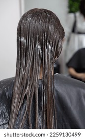 Hairdresser applies a hair mask to straight black hair. 
Hair care at the beauty salon - Shutterstock ID 2259130499