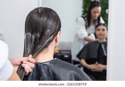 Hairdresser applies a hair mask to straight black hair. Hair care at the beauty salon. - Powered by Shutterstock