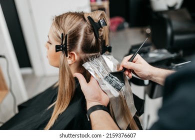 Hairdresser is applying bleaching powder on woman's hair and wrapping into the foil.  - Shutterstock ID 2159376607