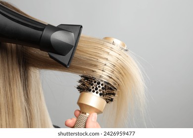 Hairdresser blow drying client's hair on light grey background, closeup - Powered by Shutterstock