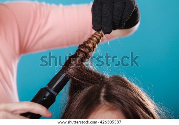 Hairdresser curling woman\
hair with electric iron curler tong. Hairstylist making girl\
hairstyle. Beauty.