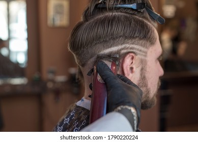 a hairdresser cuts a bearded young guy with a hair trimmer, combing the hair on his head. Work of the master in men's haircut in a barbershop - Powered by Shutterstock