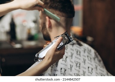 a hairdresser cuts a bearded young guy with a hair trimmer, combing the hair on his head. Work of the master in men's haircut in a barbershop - Powered by Shutterstock