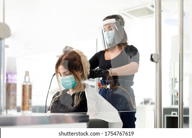 hairdresser cuts hair to a client: both are protected by surgical mask - Powered by Shutterstock