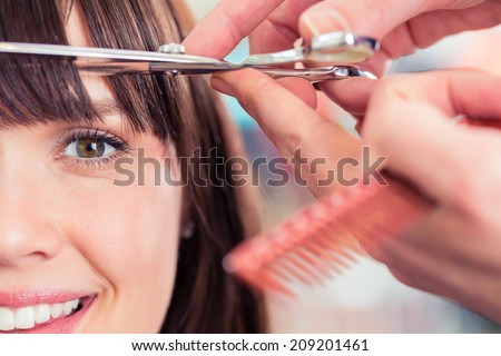 Hairdresser cutting woman bangs hair in shop
