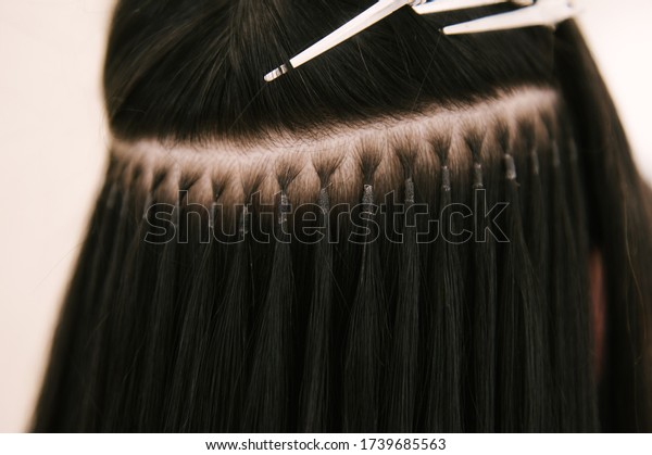 The hairdresser does hair extensions to a young girl\
in a beauty salon. Professional hair care. Close up of capsules and\
strands of grown hair