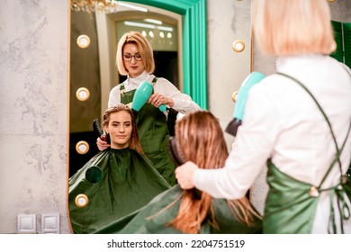 The Hairdresser Dries Hair With A Hairdryer Of The Beautiful Young Caucasian Woman In The Beauty Salon