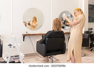 Hairdresser Drying The Hair Of A Blonde Woman In Her Hair Salon. View From Behind