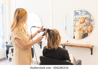 Hairdresser Drying The Hair Of A Blonde Woman In Her Hair Salon. View From Behind