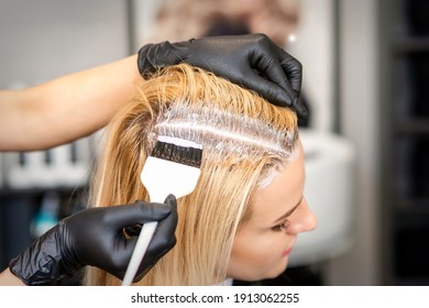 The hairdresser dyeing blonde hair roots with a brush for a young woman in a hair salon - Shutterstock ID 1913062255