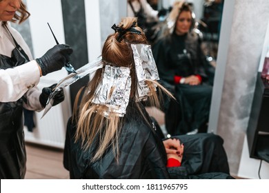 Hairdresser is dyeing female hair, making hair highlights to his client with a foil. - Powered by Shutterstock