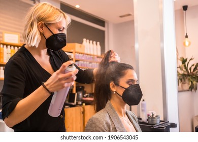 Hairdresser with face mask combing the client's hair with hairspray. Reopening with security measures of Hairdressers in the Covid-19 pandemic - Powered by Shutterstock