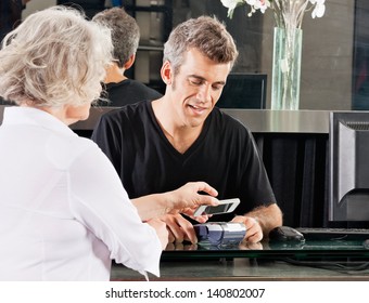 Hairdresser with female client paying with mobilephone over electronic reader at counter - Powered by Shutterstock