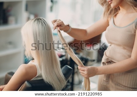 Hairdresser female making hair extensions to young woman with blonde hair in beauty salon. Professional hair extension