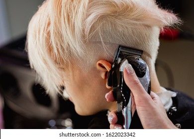 Hairdresser Machine Cuts Woman Client. A Short Haircut, Shaved Temple And A Drawing On The Hair. Dyed Hair.