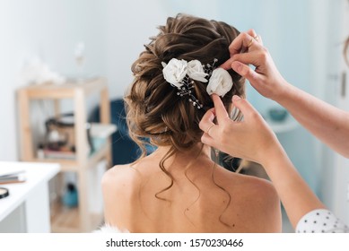 hairdresser makes an elegant hairstyle styling bride with white flowers in her hair in the salon - Powered by Shutterstock