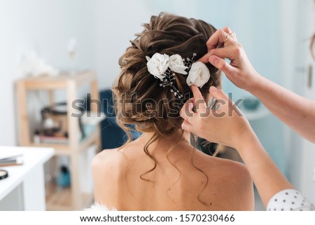 hairdresser makes an elegant hairstyle styling bride with white flowers in her hair in the salon